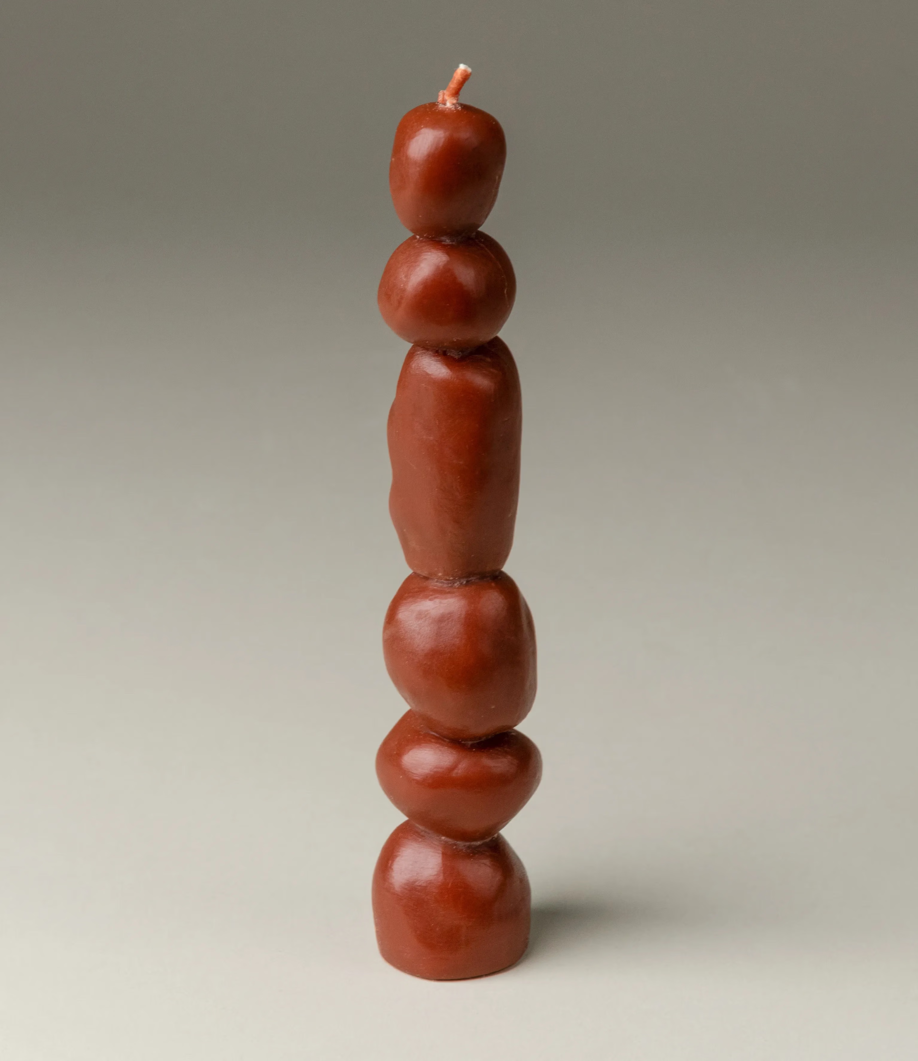 One of the three candles of Piu Set by Ann Vincent. This candle has a dark burgundy color and the shapes looks similar to little stones stacked on top of each other