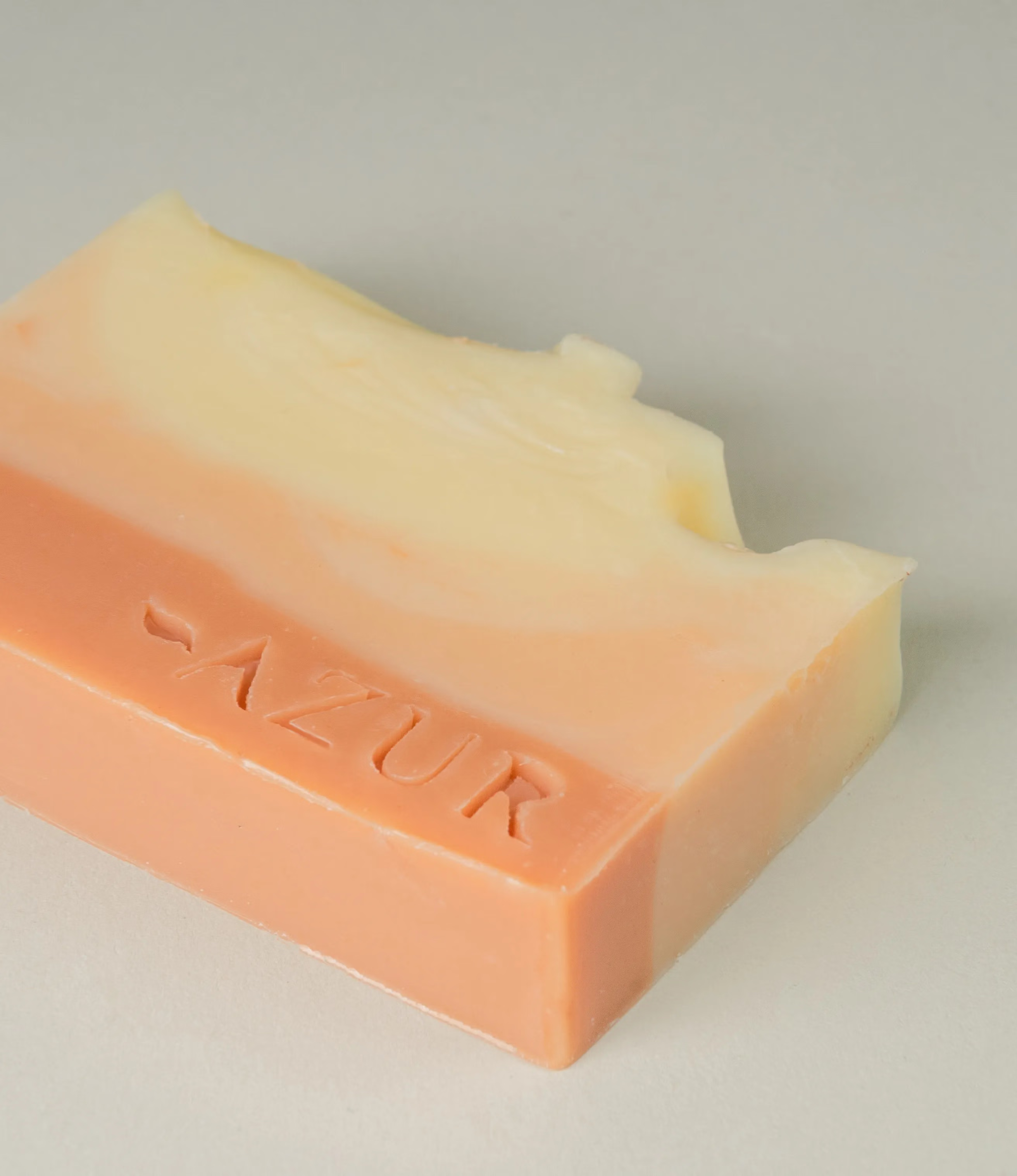 This soap has the scent of Sunset Dreams and it was crafted by Azur Natural Bodycare. The product merges shades of orange and vanilla reminding the costumer of a sunset. The top of the soap looks like the waves of the ocean. The logo of the brand appears embossed on the item.