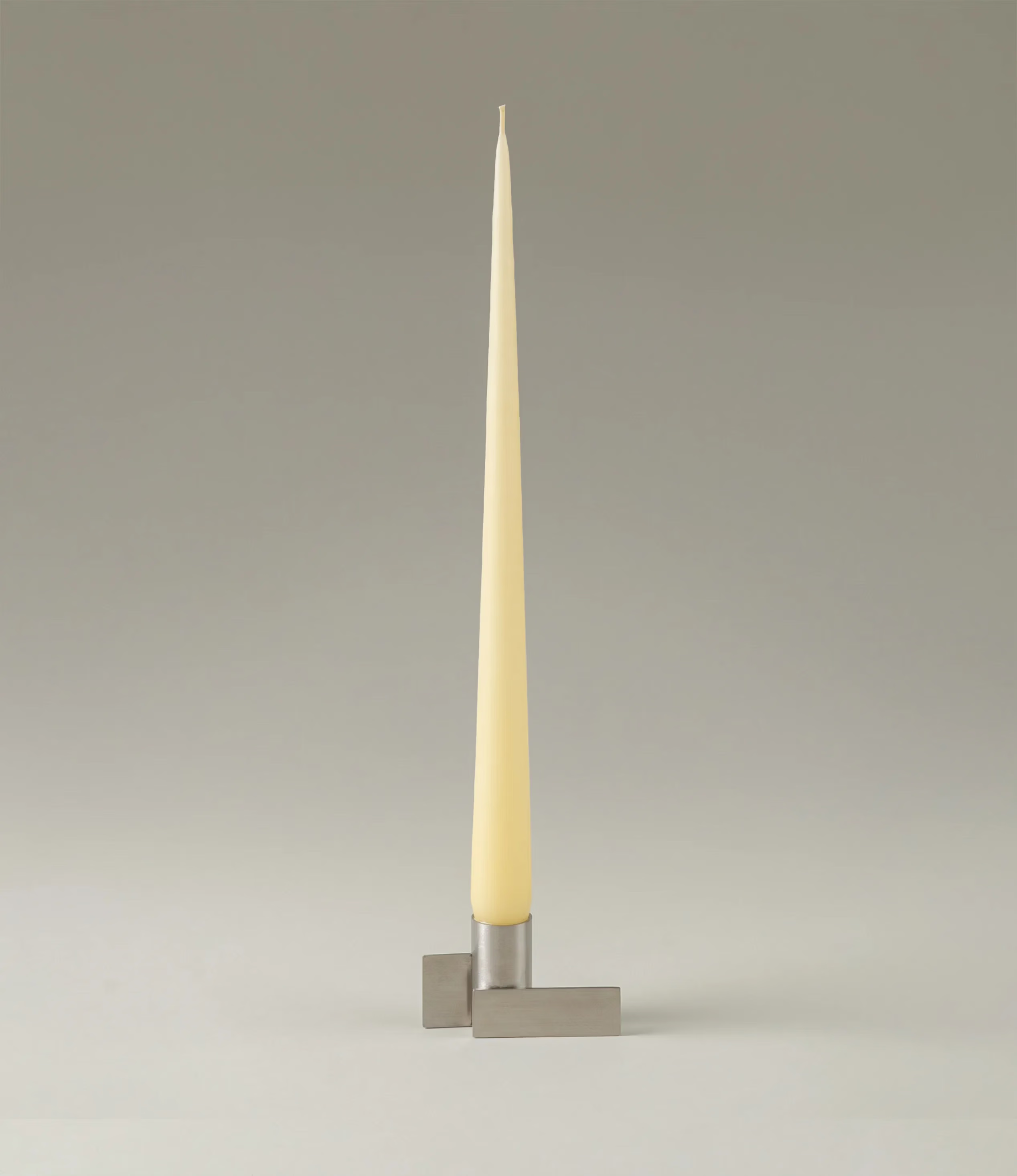 Ester&Erik Taper Candle coming in a Buttermilk shade. The product is showcased in a stainless steel Icon Candleholder from Stences.