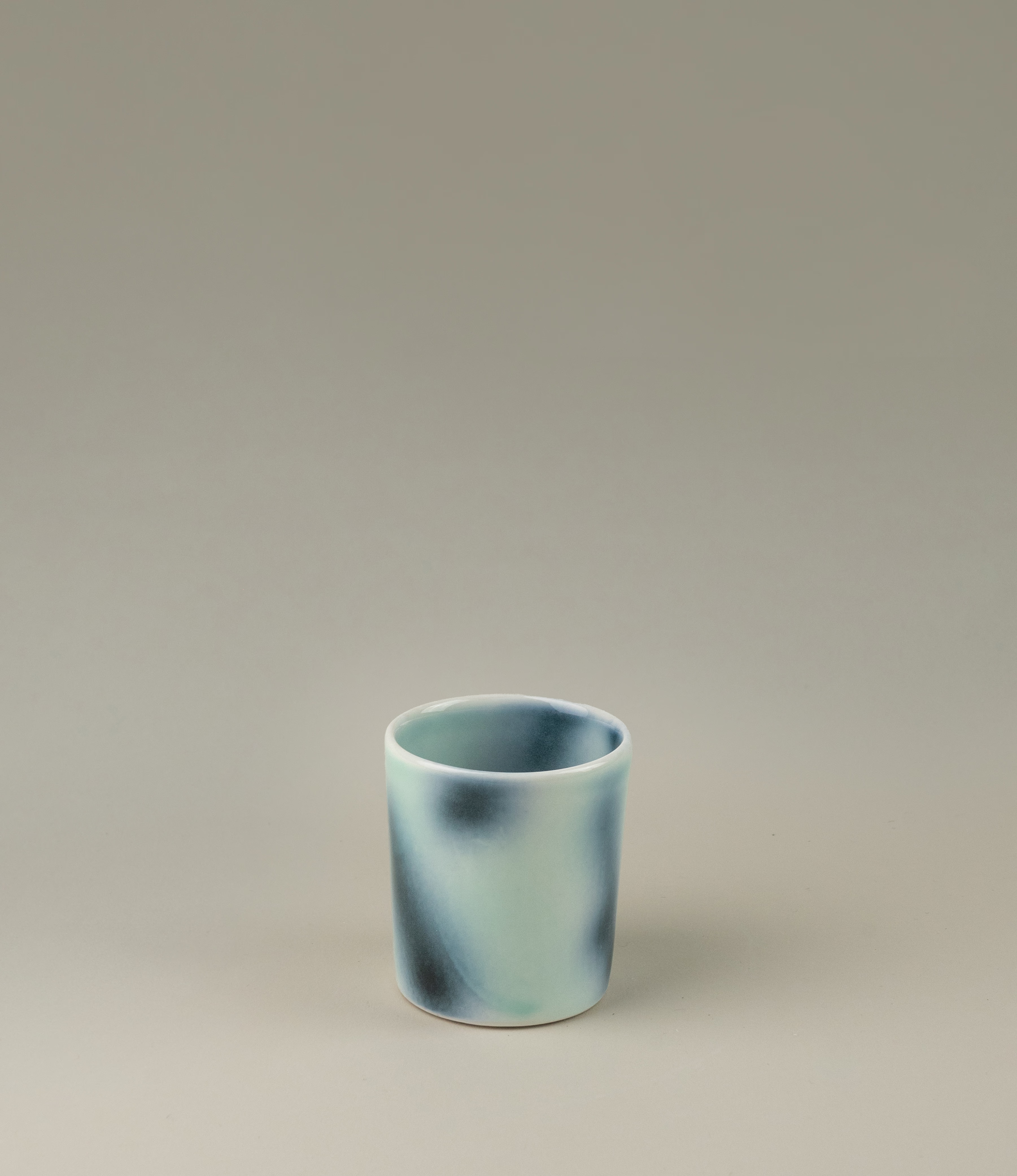 Bulle Cup from Frizbee Ceramics has a unique gradient painted pattern. The product has cold colors like green, dark and light blue. The bottom of the cup looks like it's made of small bubbles. On this picture a hand is holding the cup.