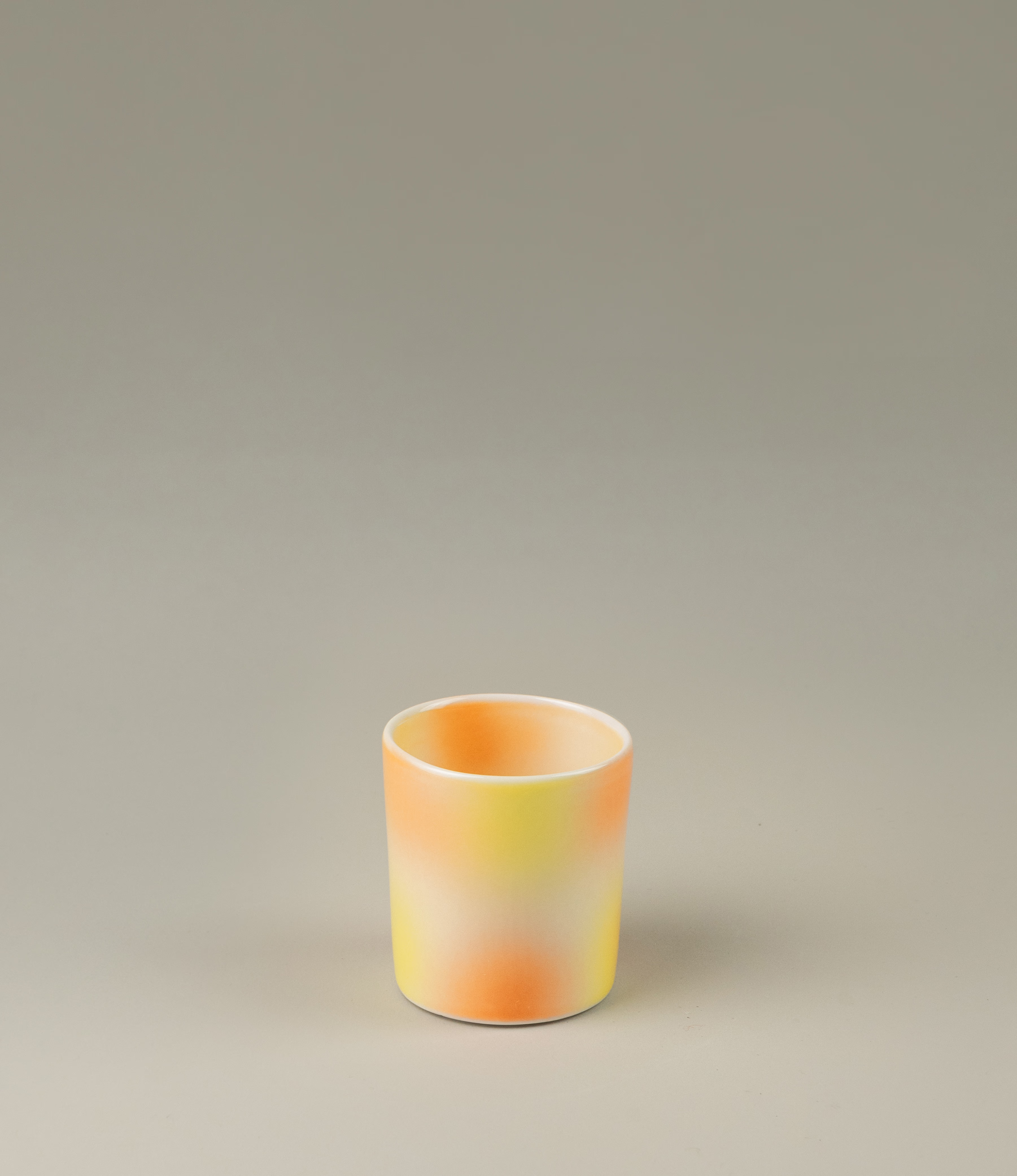 Bulle Cup from Frizbee Ceramics has a unique gradient painted pattern. The product has warm colors like orange, peach and yellow. The bottom of the cup looks like it's made of small bubbles.