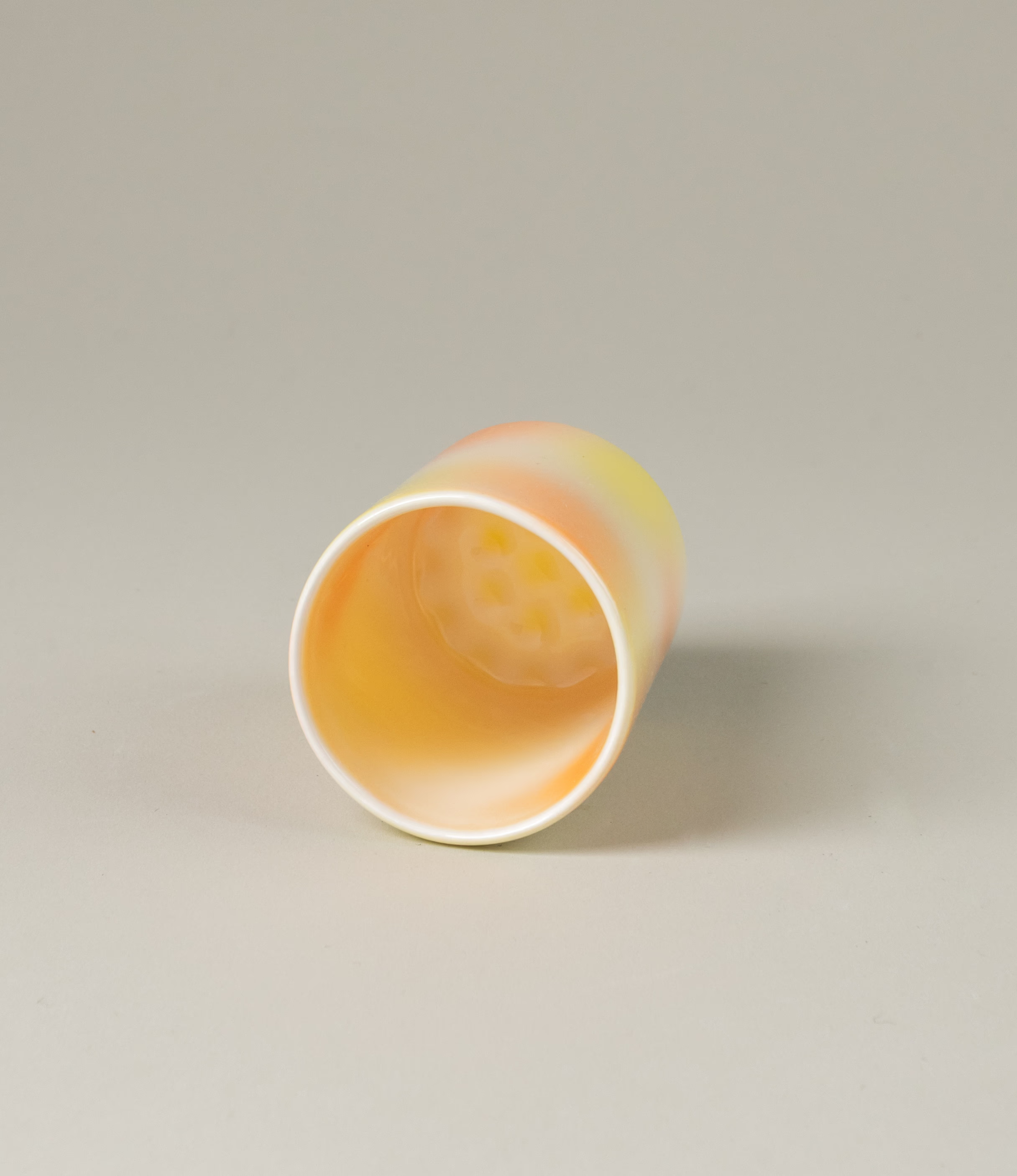 Bulle Cup from Frizbee Ceramics has a unique gradient painted pattern. The product has warm colors like orange, peach and yellow. The bottom of the cup looks like it's made of small bubbles.