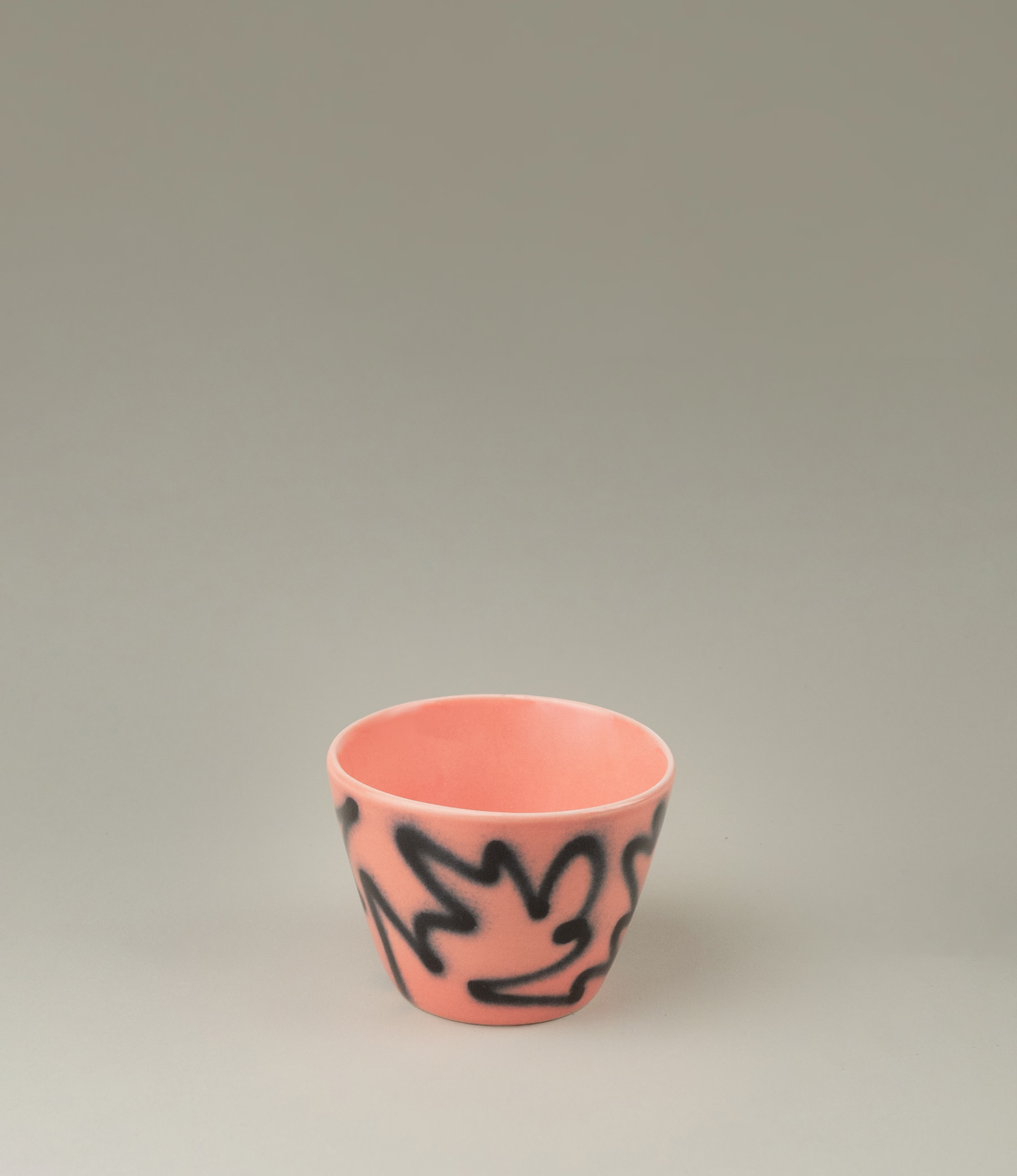 Super Cup from Frizbee Ceramics is a set of two cups. The cups' base is peach with a black graffiti like zig-zag painting on it.