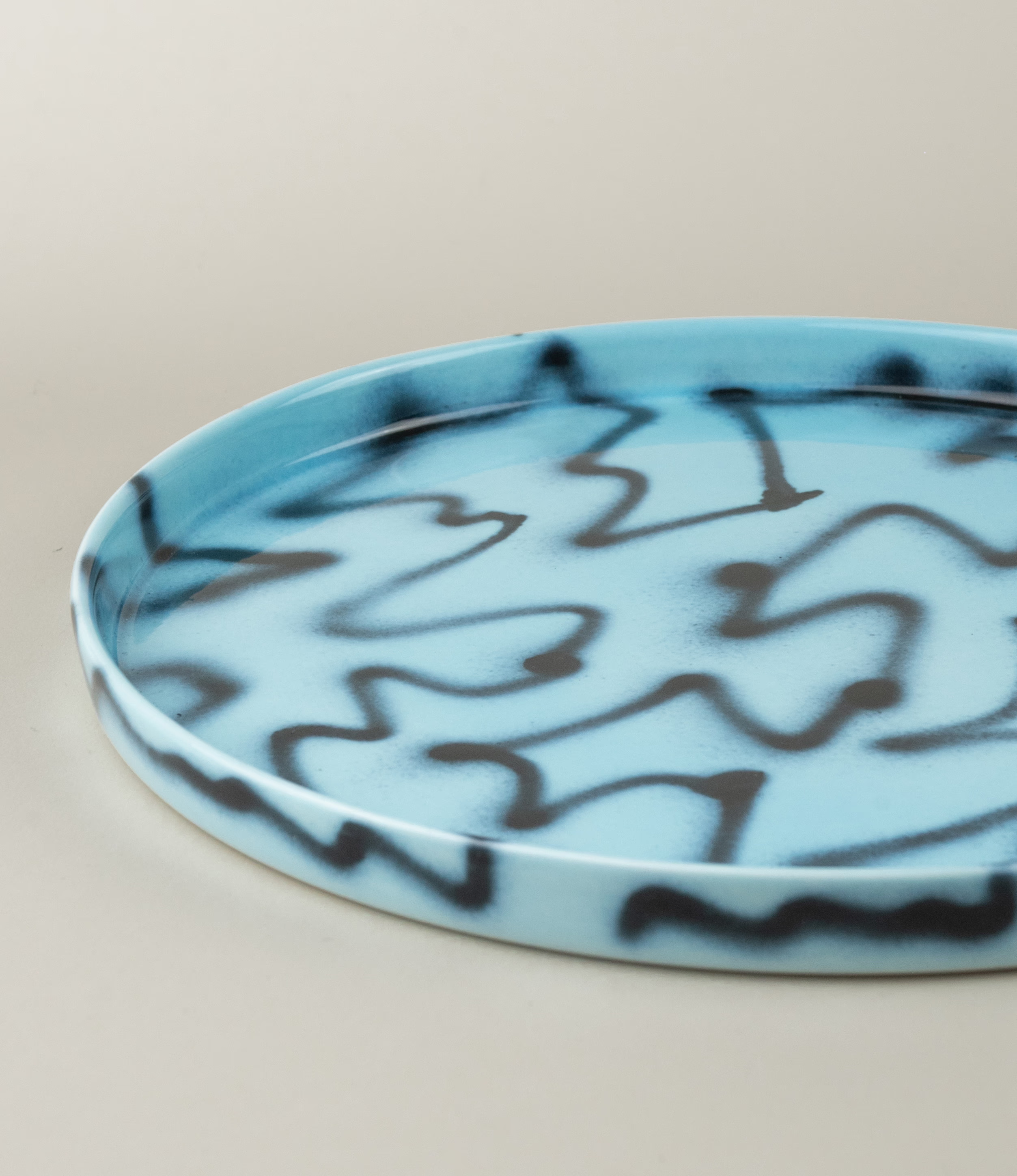 Blue Pizza Tray from Frizbee Ceramics. The tray is coming in the soothing light blue color matched with the contrasting black zig-zag pattern. The picture shows the details of the product.