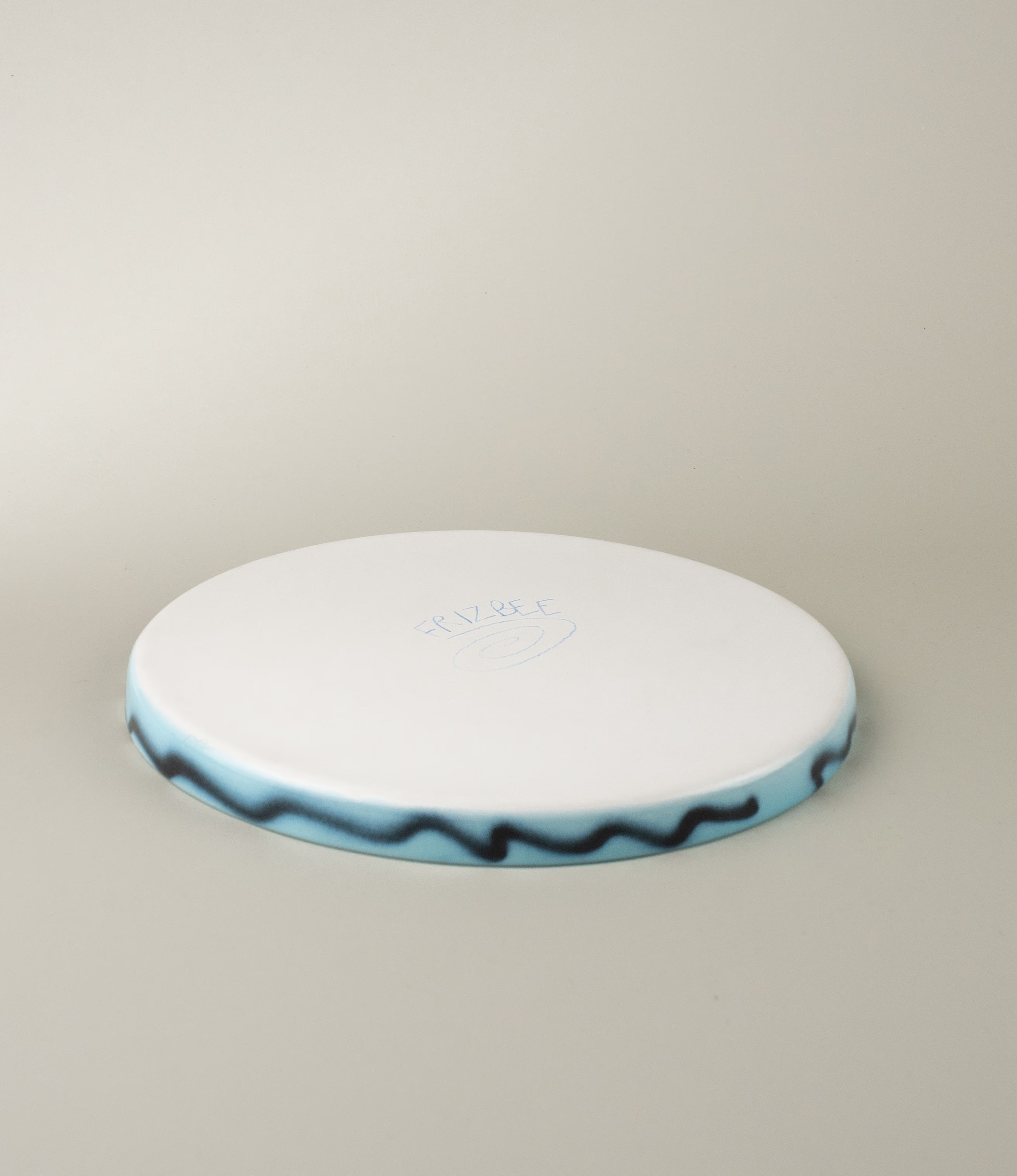 This picture shows the back and the edge of the Blue Pizza Tray. The bottom of the item is white with the hand drawn logo of Frizbee Ceramics.