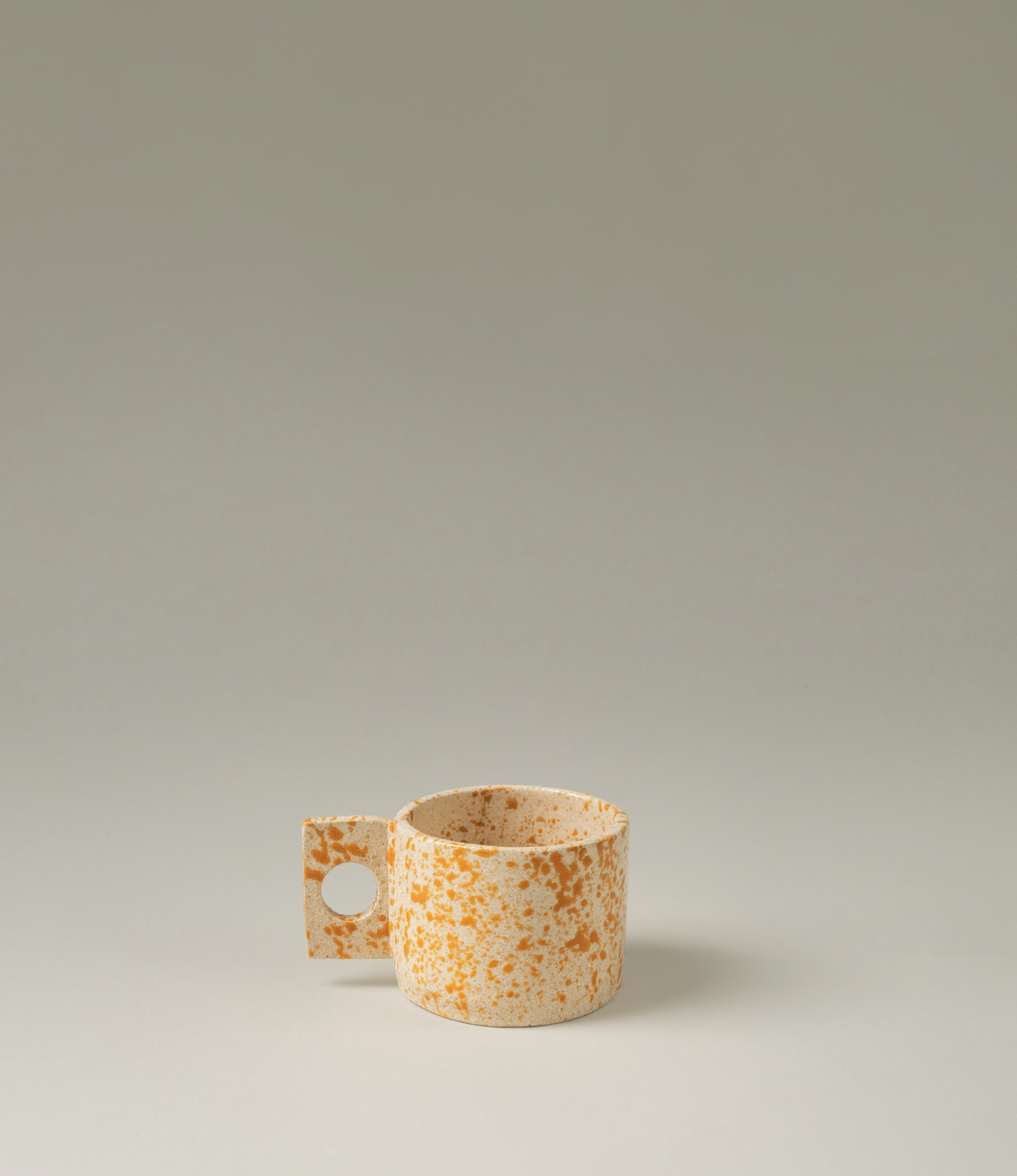 Pumpkin Spice Coffee Cup from Manamo Cups. The product has a natural touch and a modern shape with the rectangular handle. The item has a spotted orange texture on a beige base.