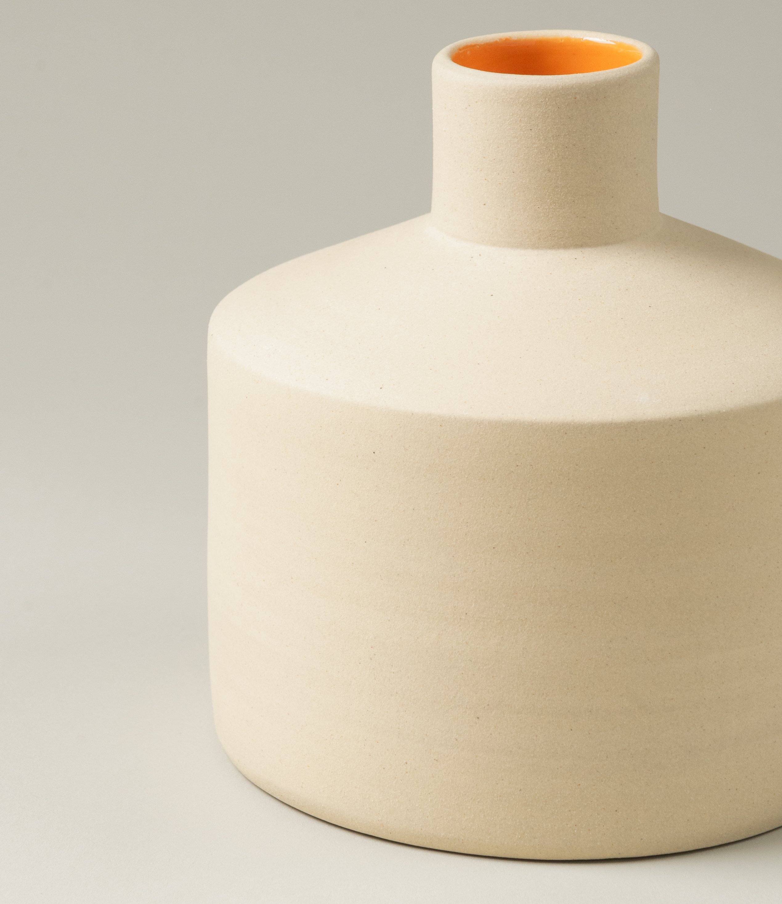 A closeup of Ocactuu's Natural Vase Orange coming in the M size. The outer side of the product has a light beige hue and the inside is glazed with an orange color.