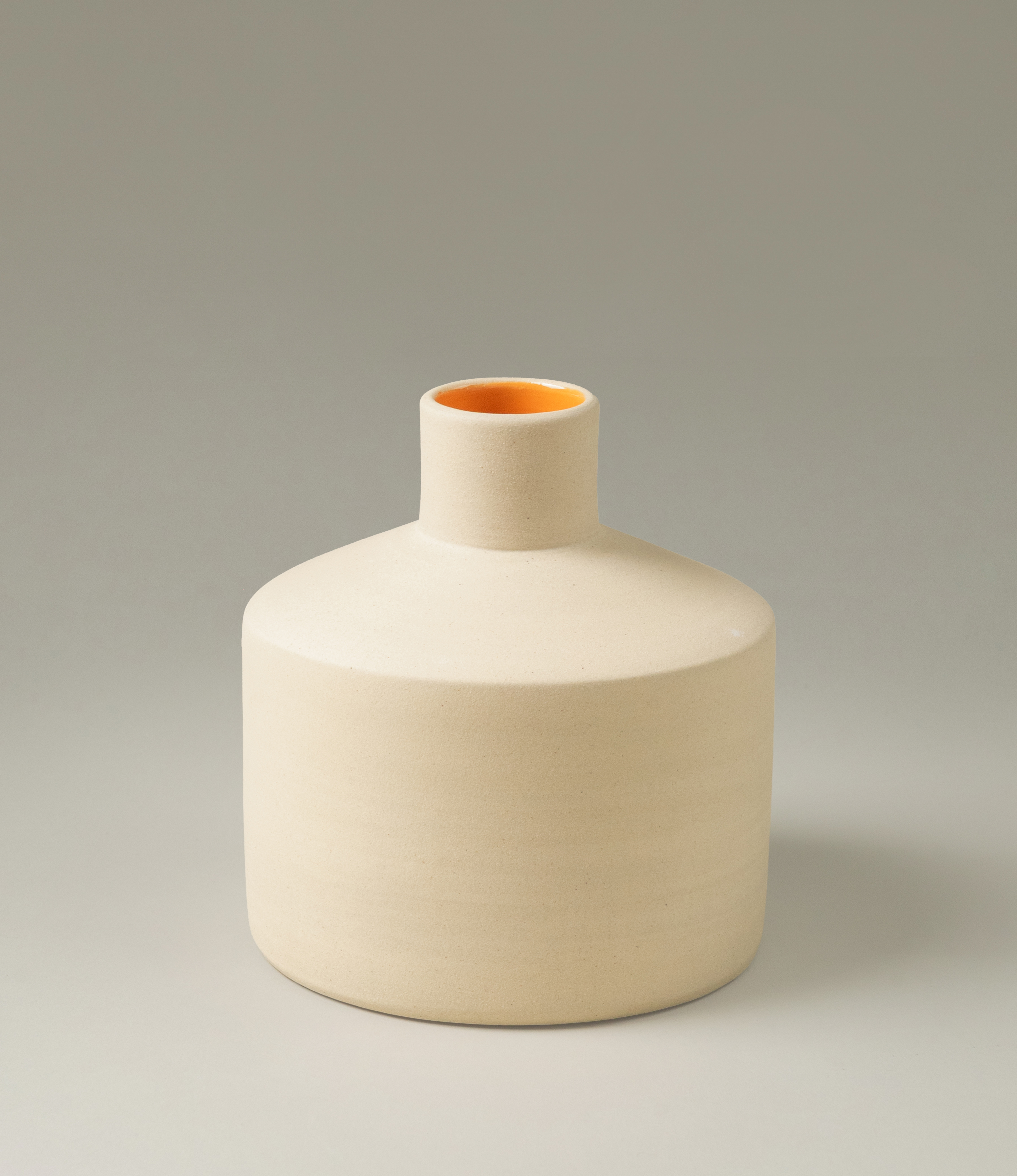 Natural Orange Vase was designed by Ocactuu. The item has a champagne color matte finish on the outside and a bright orange glossy glaze on the inside. The product is very geometrical and it has clear edges. This picture shows the M variant.