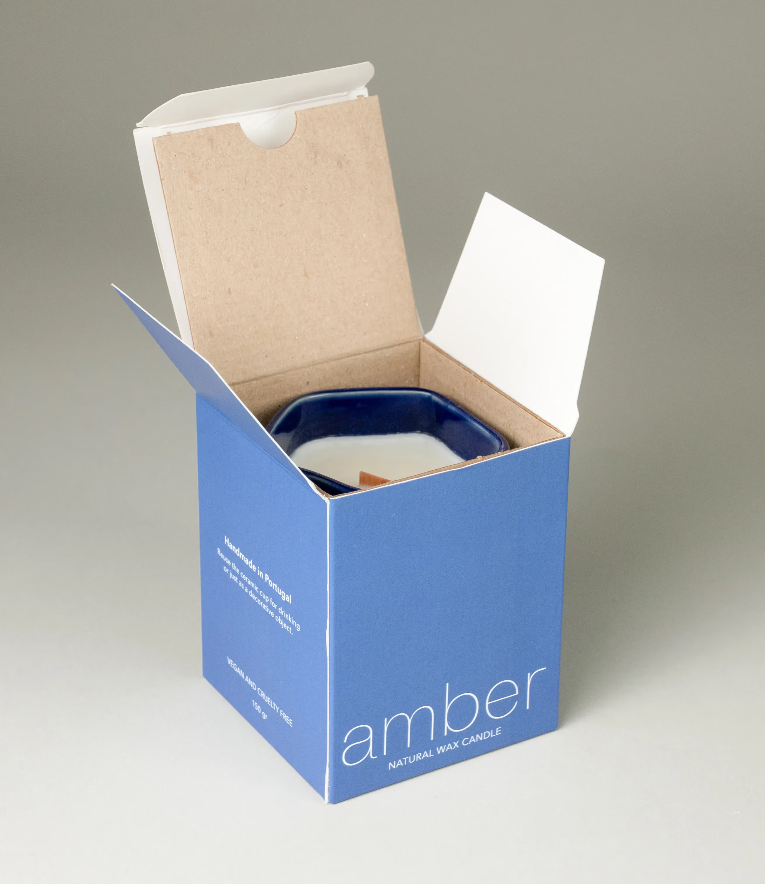 A scented Wax Candle designed by Ocactuu. The candle has an amber scent and it comes in a glossy dark blue ceramic. The packaging of the product is a minimal modern design with a blue base.