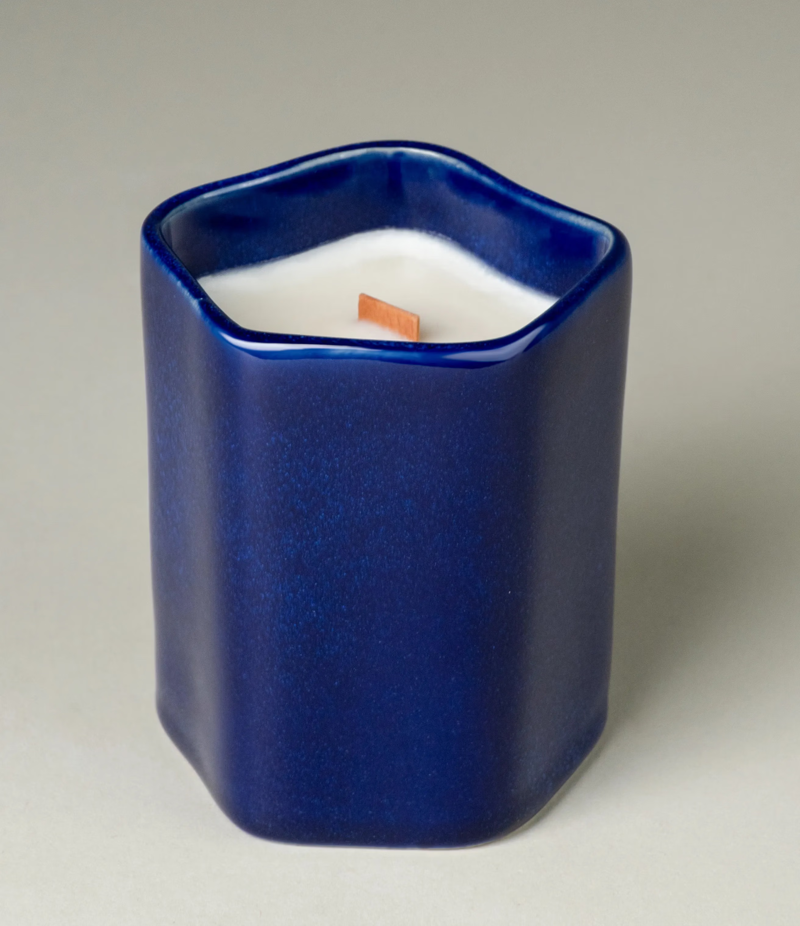 A scented Wax Candle designed by Ocactuu. The candle has an amber scent and it comes in a glossy dark blue ceramic. The material has a subtle spotted texture. The candle wick is made of wood for a more natural feeling.  