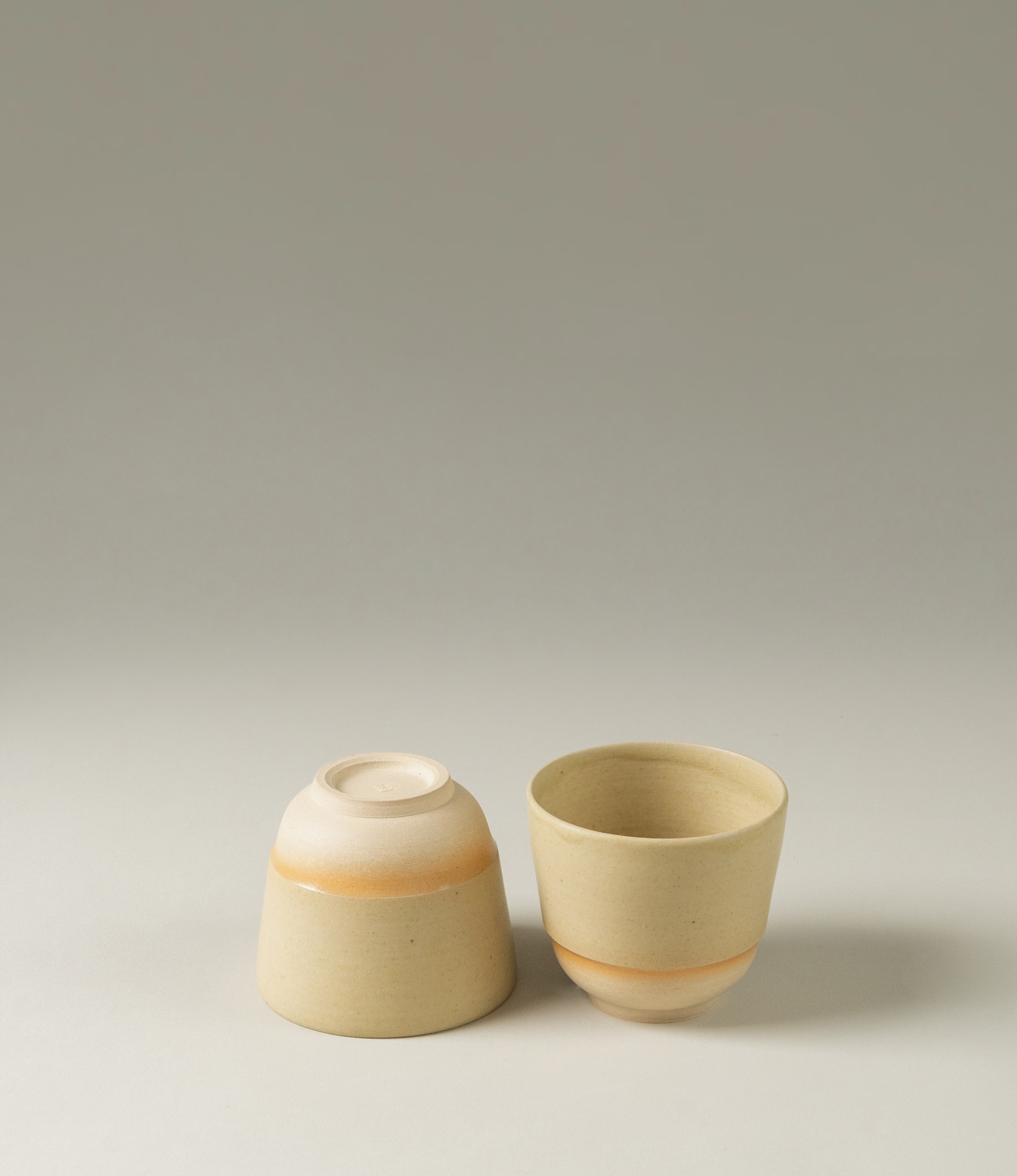 This cup set is handcrafted by Omni Ceramics. The two small cups are wearing a gradient orange color ring on the natural beige base. 