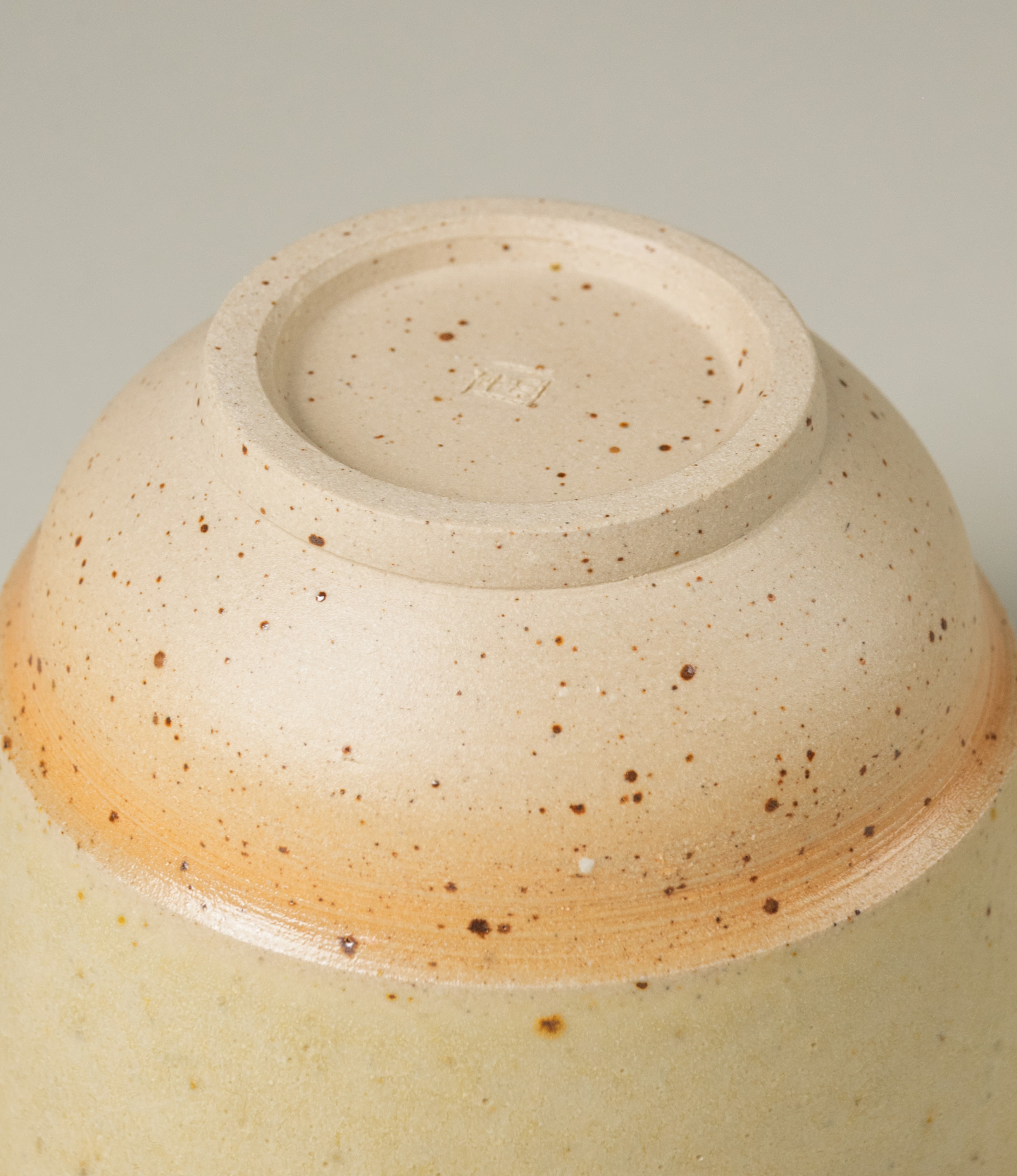 A pourer from Omni Ceramics, handmade in Belgium with an attention to detail. The bottom holds an engraved logo of the designer. The product comes in a light beige natural color, with a painted orange gradient ring and soft darker spotted pattern on the bottom part. The item is perfect to prepare your morning matcha tea.