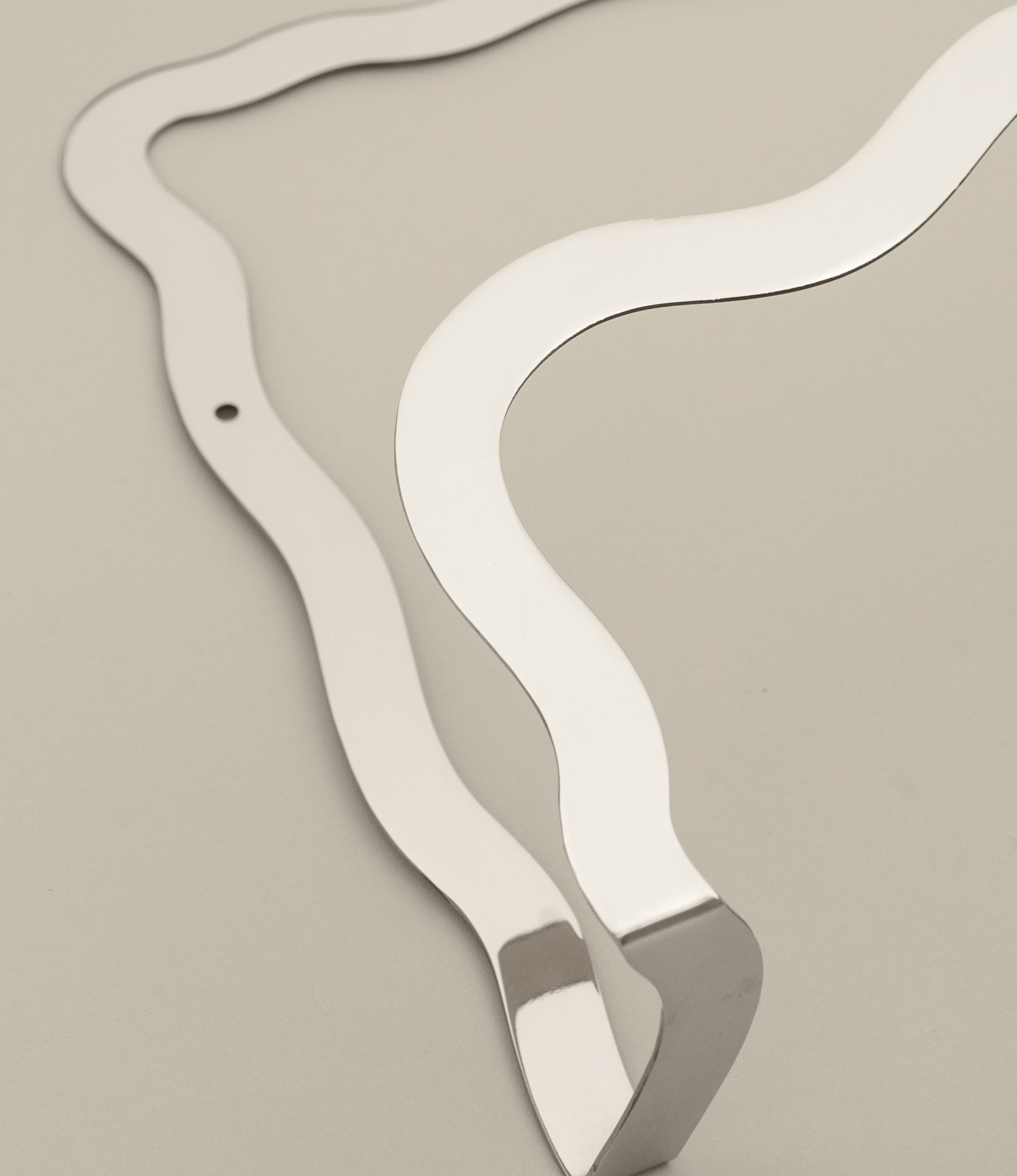 Closeup of the Wave Magazin Holder from Stences. The stainless steel piece can be attached to your wall. The wavy shape contrasts the brutalist material.